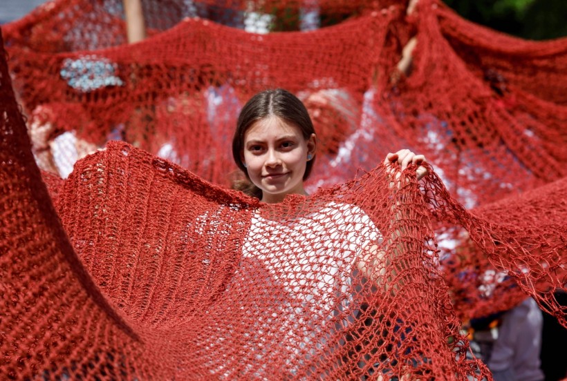 A woman carries a red long handmade crochet to represent blood alongside others during a protest to demand justice for victims of femicides and gender violence 