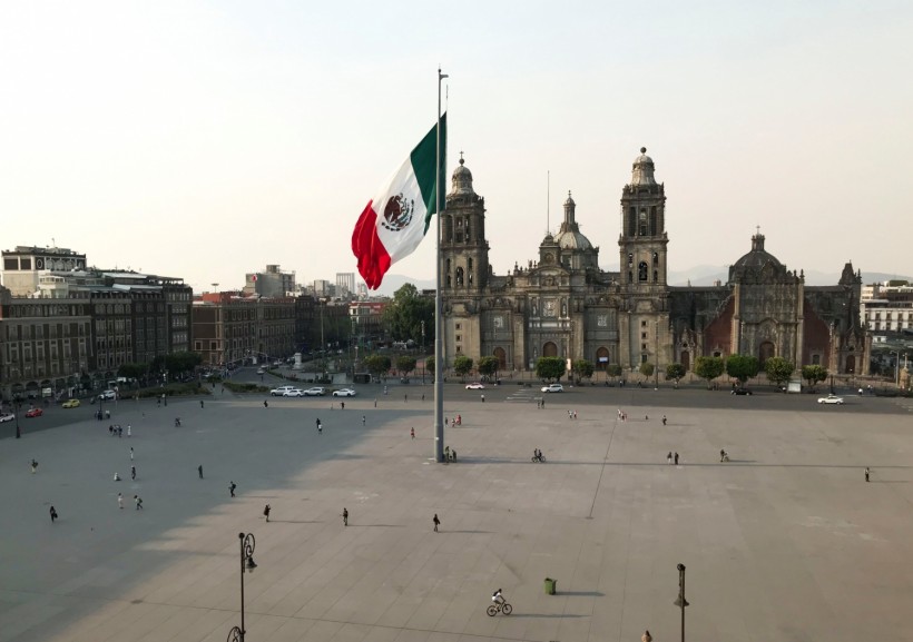 People walk near the national flag and the Metropolitan Cathedral on a Zocalo Square partially empty as the coronavirus disease (COVID-19) outbreak continues, in Mexico City