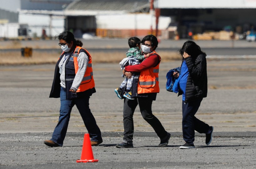 Government officials, wearing protective masks, walk along with a migrant and her son deported from the U.S. after arriving at La Aurora International airport, in Guatemala City