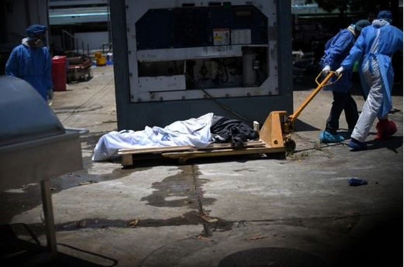 Health workers wearing protective gear bring a dead body past a refrigerated container outside of Teodoro Maldonado Carbo Hospital