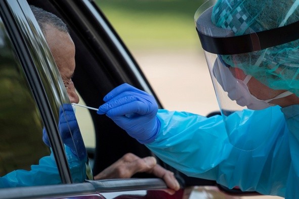 Health care worker uses a swab to test man at COVID-19 drive in testing location in Houston, Texas