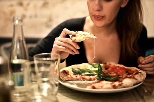Woman Hold Sliced Pizza Seats by Table with Glass