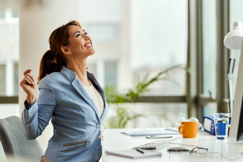 Happy female entrepreneur looking up while stretching in the office