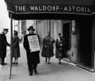 A lone hotel barber, a member of the AFL-CIO, carries a sign objecting to scab employees as he strikes outside the Waldorf-Astoria Hotel, New York City, 1940s