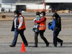 Government officials, wearing protective masks, walk along with a migrant and her son deported from the U.S. after arriving at La Aurora International airport, in Guatemala City