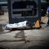 Health workers wearing protective gear bring a dead body past a refrigerated container outside of Teodoro Maldonado Carbo Hospital