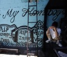 A member of the ‘Calle 18’ street gang covers his face while squatting next to a wall covered with graffiti in memory of their late members, at the prison in San Pedro Sula, Honduras, on May 28, 2013