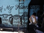 A member of the ‘Calle 18’ street gang covers his face while squatting next to a wall covered with graffiti in memory of their late members, at the prison in San Pedro Sula, Honduras, on May 28, 2013