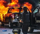 A police officer stands near a burning police vehicle after demonstrators set it on fire during a protest