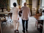 An elderly resident walks with the help of a nurse